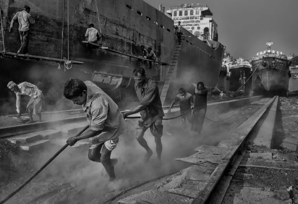 Fotografie ze souboru finalisty kategorie Cestovatelské portfolio: Dháka, Bangladéš. Ve slumu Char Kaliganj jsou v provozu jedny z největších loděnic v Asii. Věk místních zaměstnanců je od 8 do 80 let a všichni tady pracují společně.
