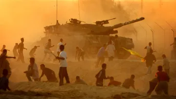 Palestinci házejí kameny na izraelský tank při střetech před zbořenou židovskou osadou Neve Dekalim na jihu Pásma Gazy. Foceno 6. září 2005