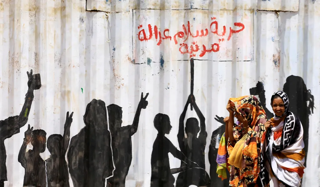 Civilisté chodí kolem graffiti, kde je v arabštině napsáno „Svoboda, mír, spravedlnost a občanství“, v konflikty zmítaném Súdánu. Fotografie je ze čtvrti Burri v Chartúmu