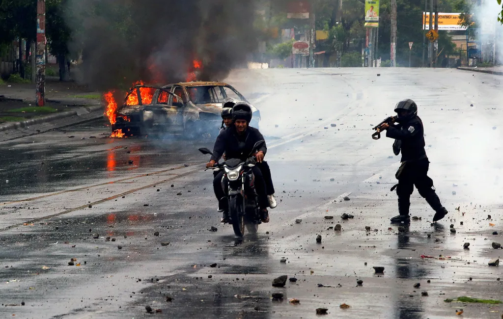 Příslušník nikaragujské speciální zásahové jednotky střílí na dva muže projíždějící na motorce ulicemi Managuy během protestů proti prezidentu Danielu Ortegovi a jeho vládě.