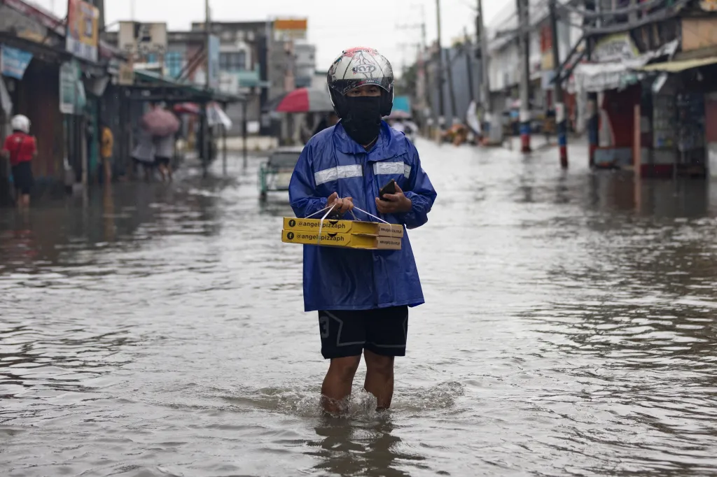 Rozvozce s krabicemi pizzy se brodí zaplavenou ulicí po tajfunu Doksuri ve Valenzuele