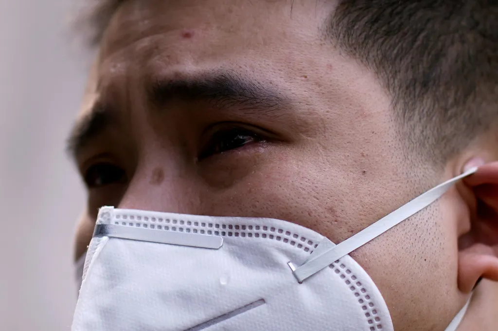 Muž s maskou na obličeji truchlí za zemřelé, kteří podlehli nákaze koronavirem