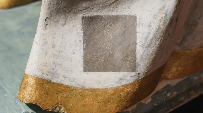 Na zadní straně pláště je zachován původní stav sochy před jejím restaurováním