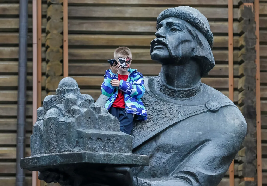 Halloween už pronikl i na Ukrajinu. Chlapec, který byl součástí zombie průvodu, se usadil s mobilem na jedné z kyjevských skulptur