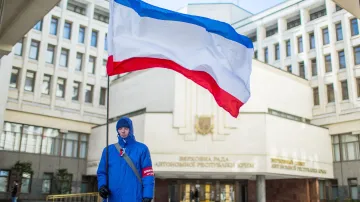 Muž s krymskou vlajkou před budovou krymského parlamentu