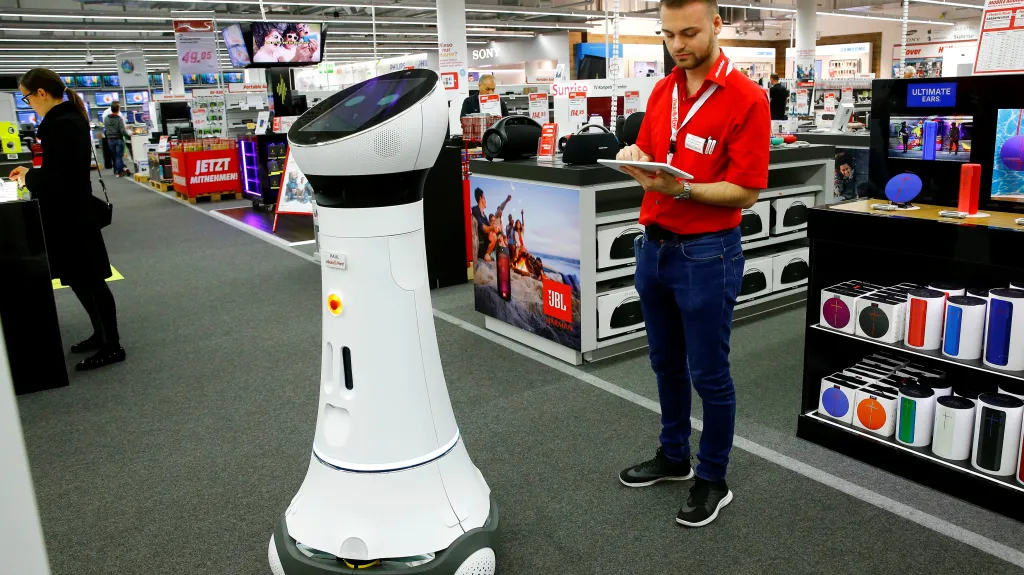 Zaměstnanec s tabletem kontroluje robota, který zákazníkům například pomáhá najít zboží (Švýcarsko)
