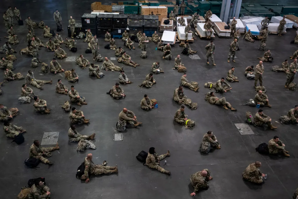 Příslušníci armády sedí v bezpečných rozestupech v prostoru budovy, kterou mají proměnit v polní nemocnici pro nakažené koronavirem