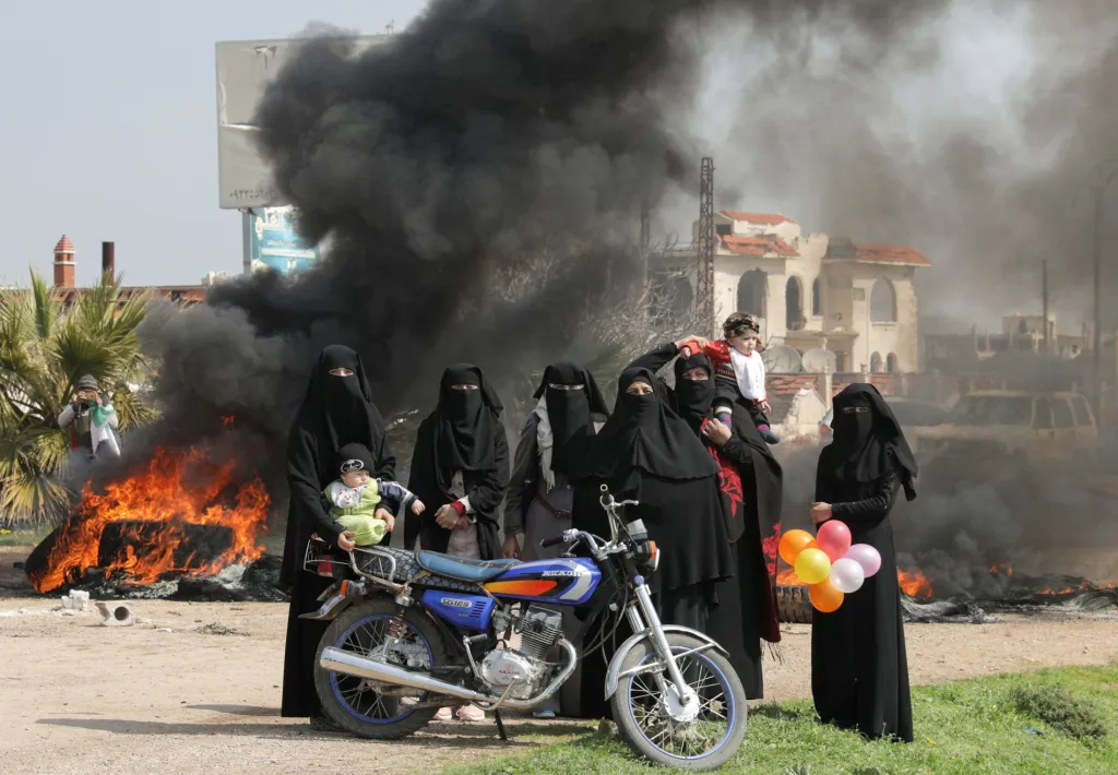 Ženy stojí poblíž hořících pneumatik během protestu proti společným rusko-tureckým vojenským hlídkám, které operují v oblasti syrského Idlibu