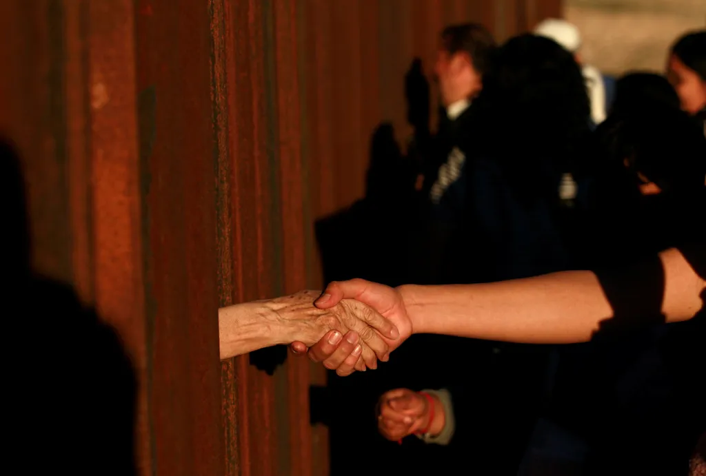 Lidé si podávají ruce přes hraniční plot mezi USA a Mexikem během bohoslužby ve městě Ciudad Juárez