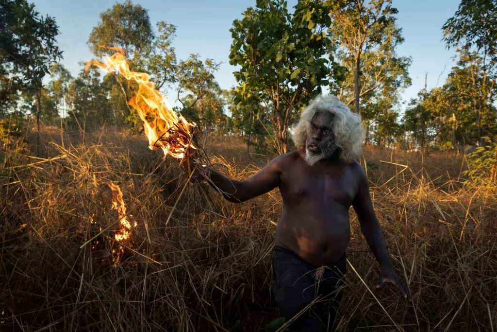 Vítězná fotografie v kategorii Fotografická série roku. Conrad Maralngurra z Nawarddekenu vypaluje trávu takzvaným „studeným pálením“, aby ochránil komunitu Mamadawerre před australskými požáry. Večerní požár přirozeně uhasne, jakmile teplota klesne a zvýší se vlhkost. Jeho předci to tak dělali tisíce let