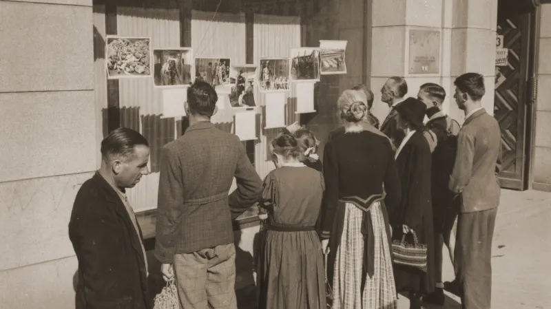 Kolemjdoucí před výlohou obchodu, kde americká armáda vystavuje fotografie z koncentračních táborů (Linec, květen 1945)