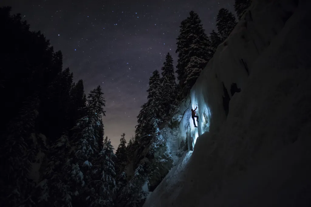 Člen horolezeckého týmu Arnicare na ledopádu během nočního tréninku pod hvězdnou oblohou nedaleko švýcarského jezera Hongrin