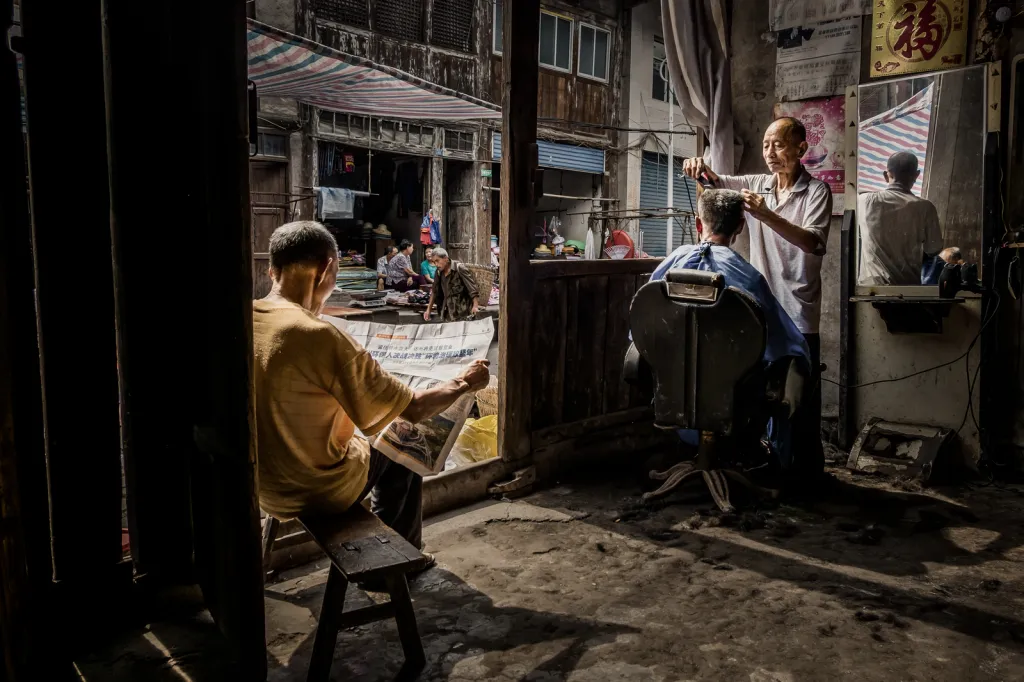 Okno (kategorie Pouliční fotografie). „Snímek byl pořízen ve starém holičství v mém rodném městě Panshi v Číně. Lidé zde stále žijí tradičním stylem, posedávají na ulici a život plyne klidným tempem, což mi připomíná dětství.“