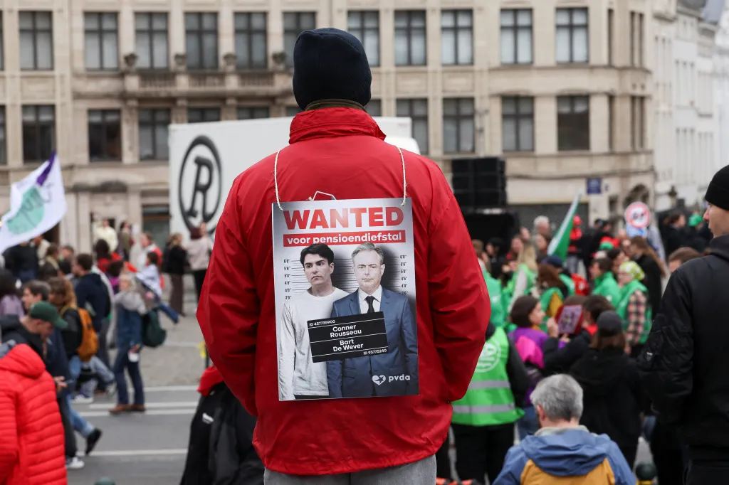 Demonstrant s transparentem zobrazujícím belgického premiéra Barta De Wevera (vpravo) a politika Connera Rousseaua (vlevo) s nápisem „Hledán za krádež důchodů"