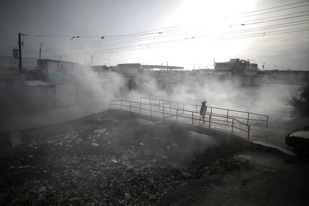 Žena kráčející kouřem z hořících odpadků ve městě Port-au-Prince na Haiti