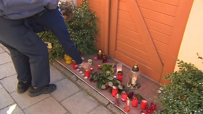 Lidé před dům pokládají květiny a zapalují svíčky