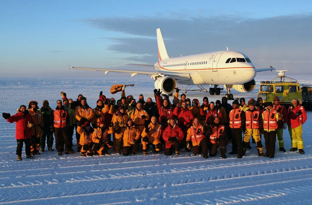 Cestující, vědci, vládní úředníci a pozemní posádka pózují na skupinové fotografii na Wilkinsově ledově modré dráze před letadlem Airbus A319, které začalo s přepravou cestujících na první komerční lince na světě z Hobartu do Antarktidy, asi 65 km od australské antarktické výzkumné stanice Casey (leden 2008)