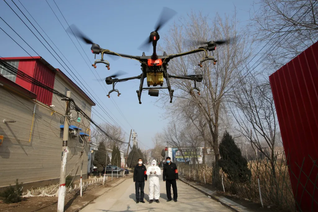 Dobrovolníci v ochranných oblecích kontrolují let dronu, který stříká dezinfekční prostředky ve vesnici Čeng-wan v provincii Chu-pej v Číně, kde propuklo onemocnění koronavirem