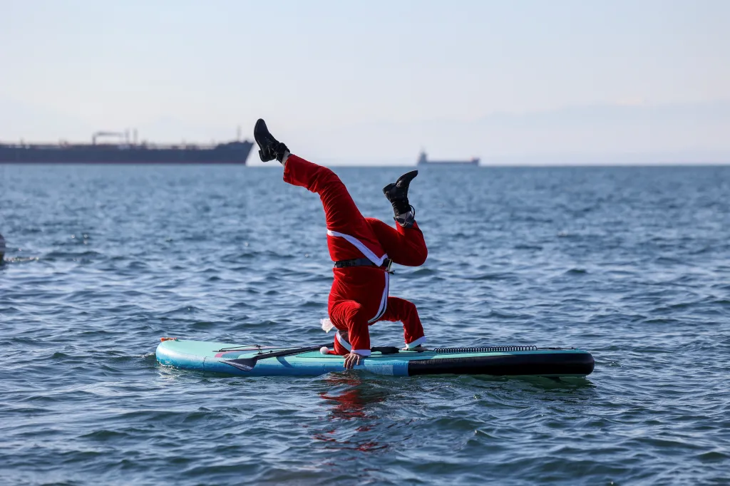 Člen paddleboardového týmu v kostýmu Santa Clause balancuje na prkně v řecké Soluni