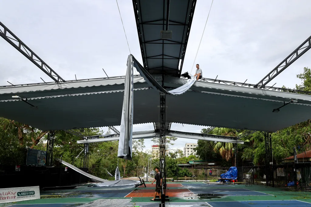 Dělník sedí na poškozené střeše tenisového kurtu