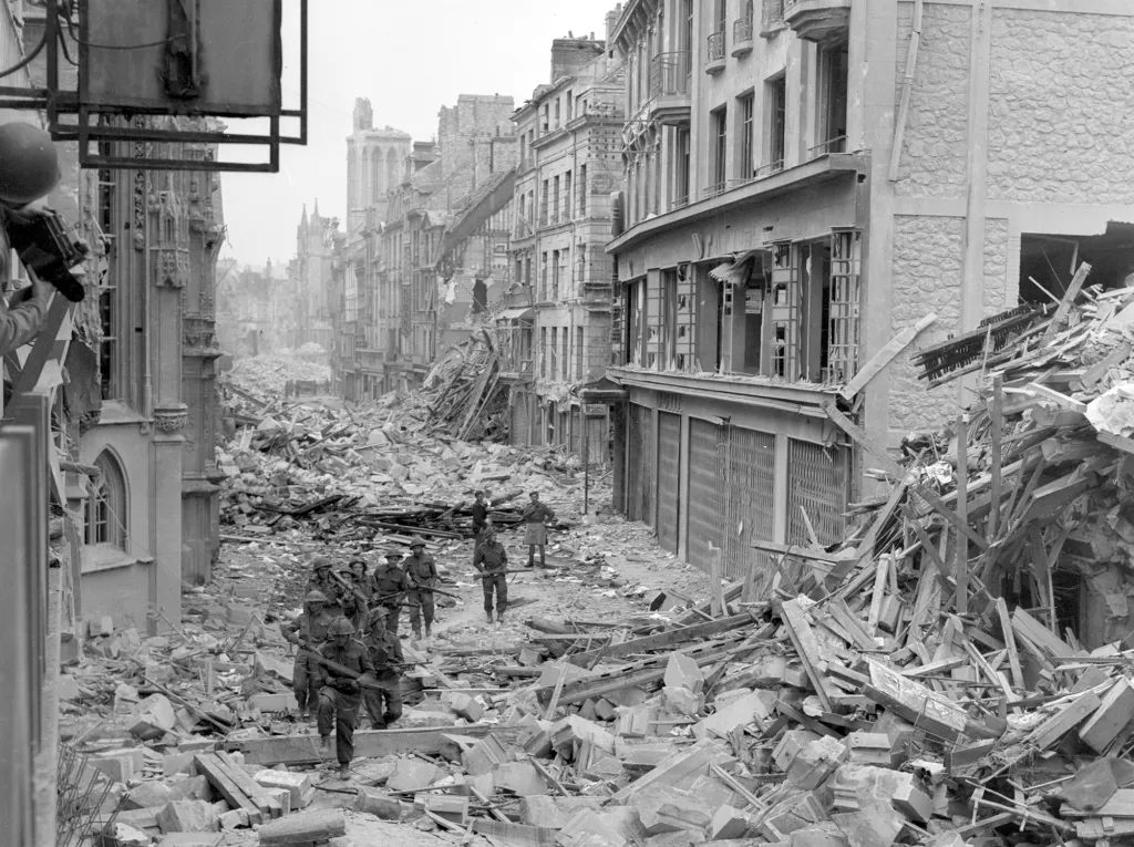 Kanadská hlídka zajišťuje oblast podél zničené Rue Saint-Pierre poté, co byly německé síly vytlačeny z města Caen. Britští a kanadští vojáci bojovali proti zesíleným německým  jednotkám v oblasti kolem Caen asi dva měsíce po přistání v Normandii