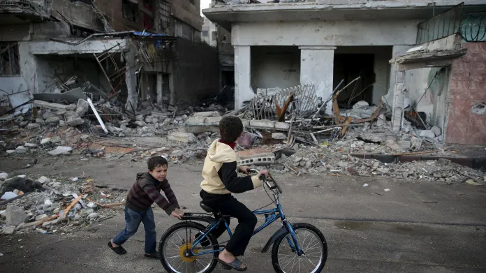 Děti si hrají na kole v blízkosti poškozených budov na předměstí Douma u Damašku