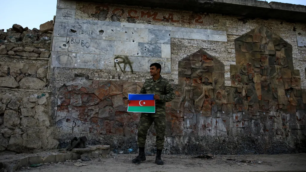 Ázerbájdžánský voják pózuje se státní vlajkou u vchodu do města Džabrajil v Náhorním Karabachu (snímek z roku 2020)