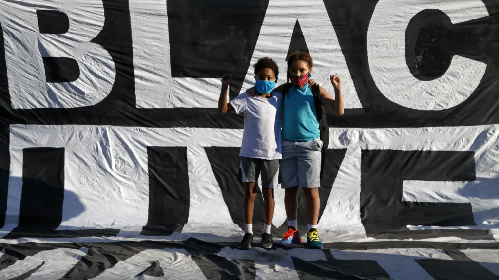 Dva chlapci stojící na transparentu hnutí Black Lives Matter, které v roce 2020 protestovalo za práva Afroameričanů v USA