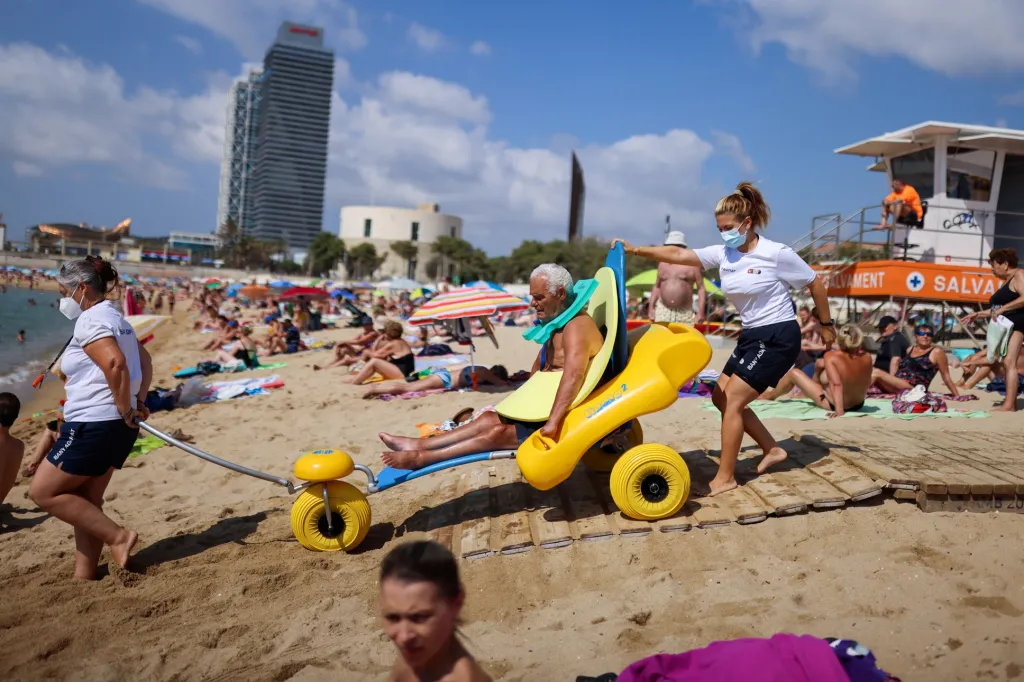 Plavčíci z pláže Nova Icaria ve Španělsku pomáhají lidem se zdravotním postižením s plaváním v moři