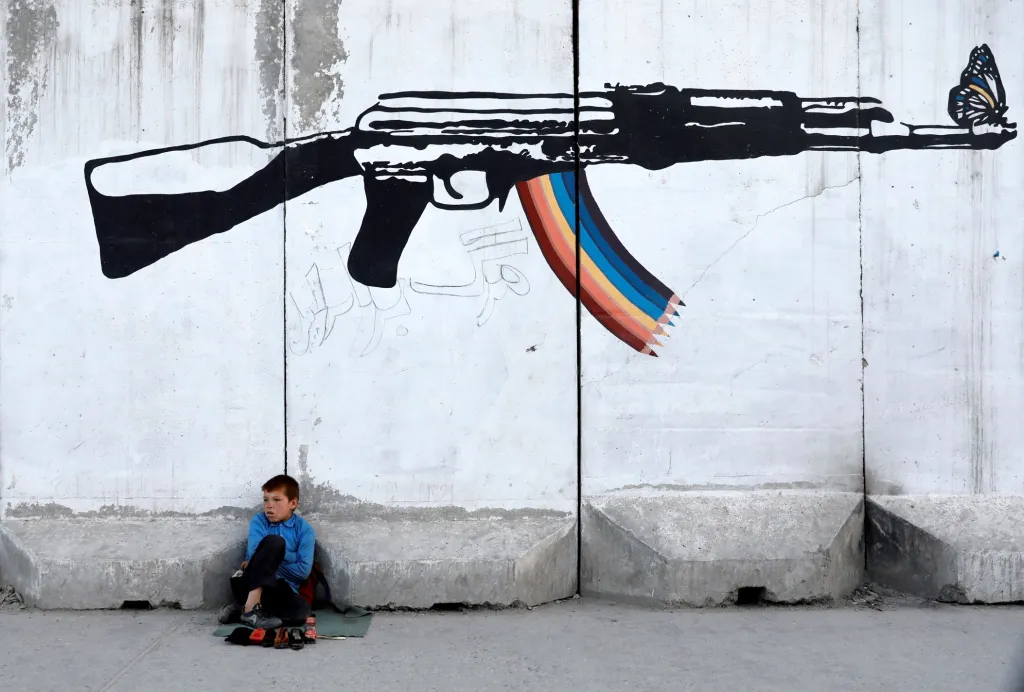Práce dětí na ulicích je přítomná i v 21. století. Na snímku je leštič bot z Kábulu, který čeká na zákazníky u stěny dekorované graffiti