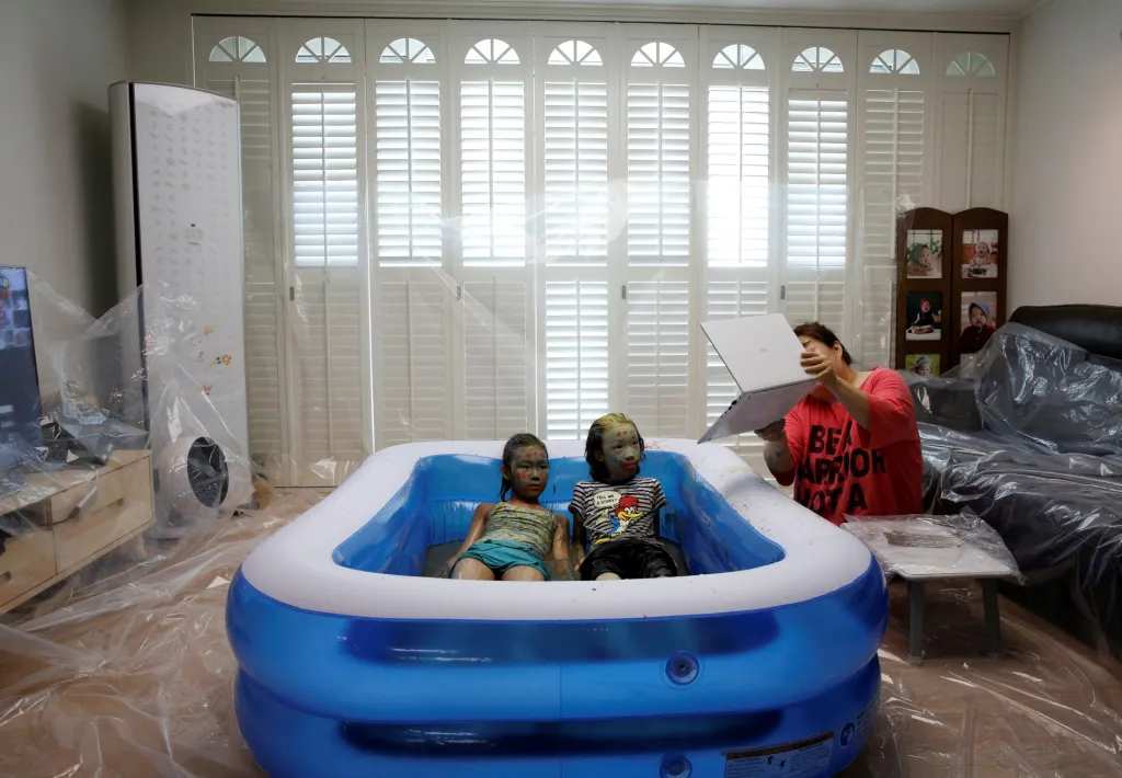 Děti si hrají v obývacím pokoji v bazénu během on-line vysílání zábavného jihokorejského festivalu bahna nazvaného Boryeong