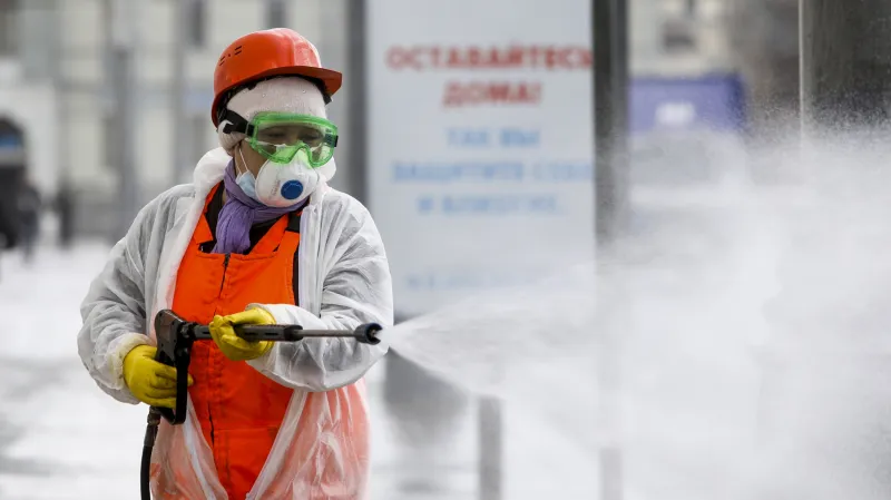 Dezinfekce ulice v Moskvě. V pozadí cedule s nápisem "Zůstaňte doma, pečujte o sebe a své milované
