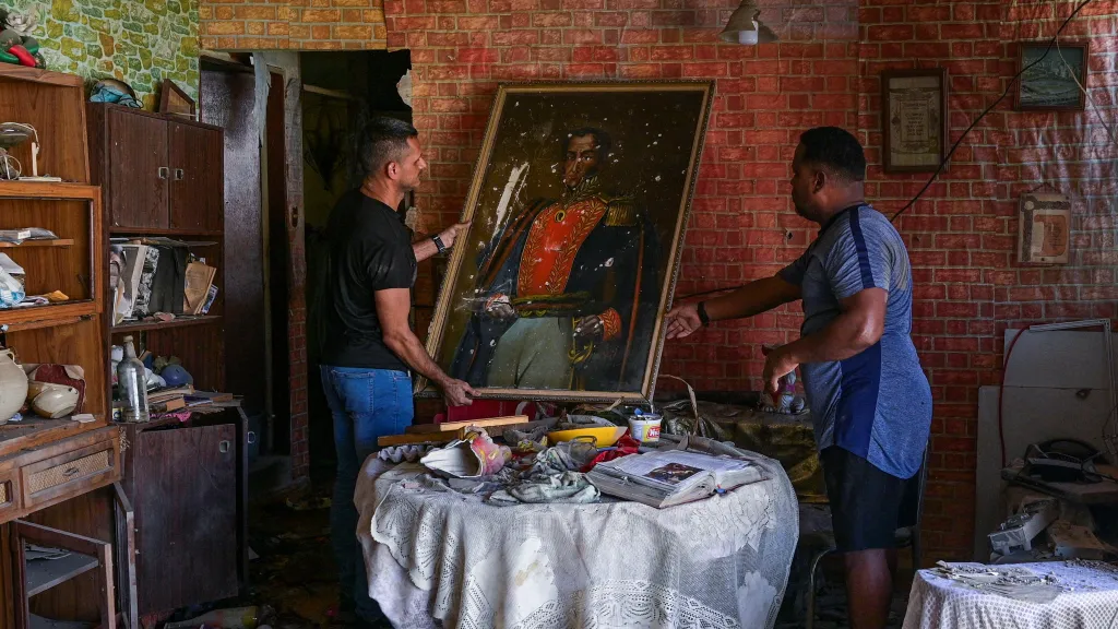 Dva Venezuelané, Jesus Linares a Reggie Carrera, manipulují s obrazem Simóna Bolívara v bytě poškozeném americkými údery
