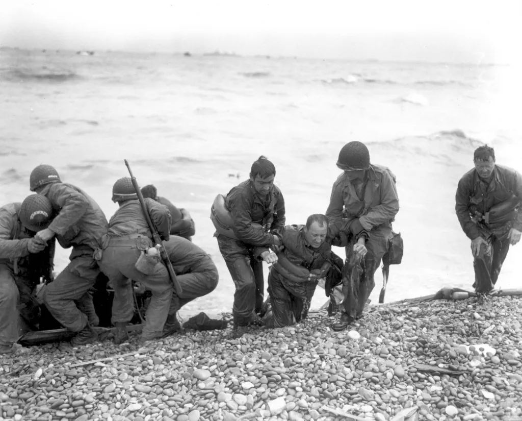 Členové amerického týmu určeného pro vylodění pomáhají vojákům, jejichž plavidlo bylo potopeno nepřátelskou palbou u pláže Omaha v blízkosti Colleville sur Mer