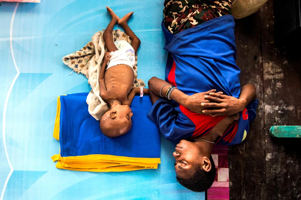 Matka se svým tříletým nemocným dítětem spí v protestantském kostele ve městě Agats poté, co vláda odeslala vojenskou a zdravotní pomoc do vzdálených oblastí Papui v rámci boje s podvýživou a spalničkami