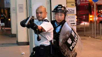 Policejní důstojník míří zbraň proti demonstrantům, kteří obklíčili policejní stanici. Na ní se nachází demonstranti zadržení během střetů v Hongkongu.