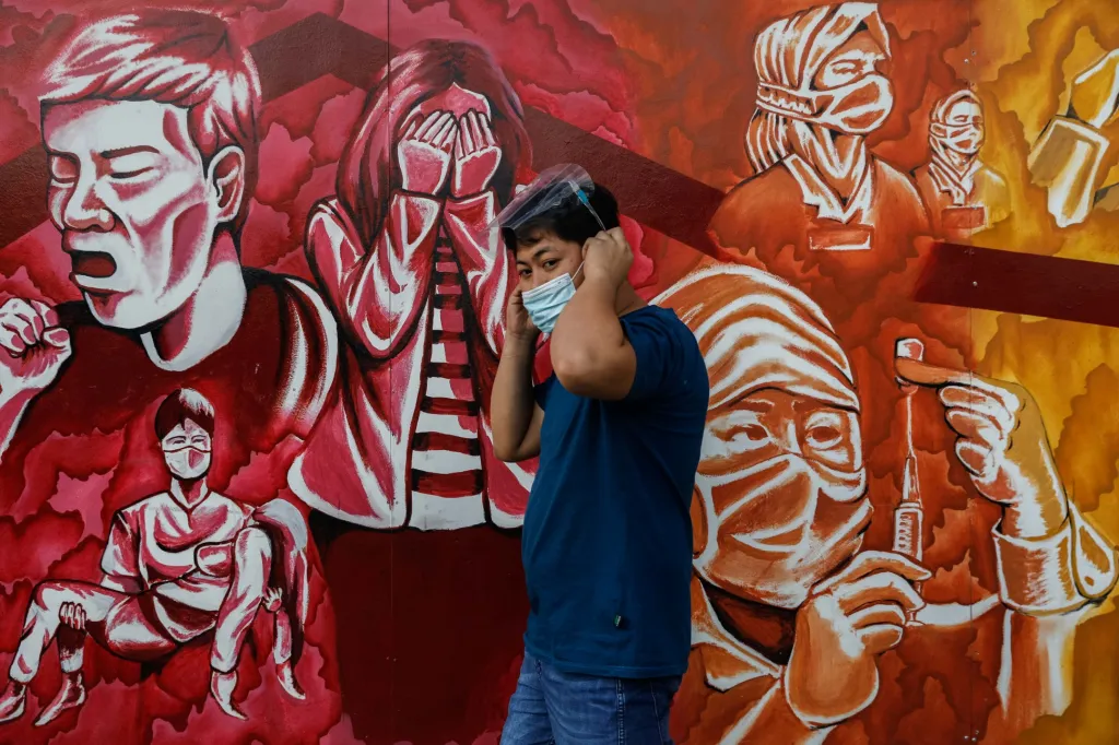 Muž si nasazuje ochrannou roušku, když prochází kolem nástěnné malby věnované zdravotnickým pracovníkům v Pasig City na Filipínách