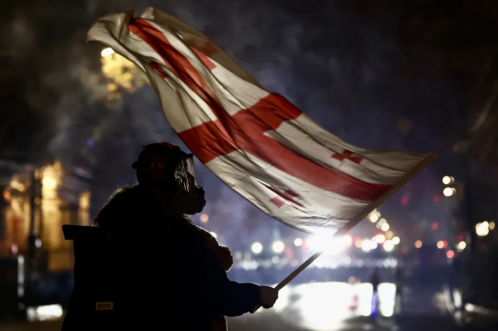Protesty v Gruzii (Protests in Georgia) – Protestující s obřím medvídkem mává během protivládního shromáždění gruzínskou vlajkou před parlamentem v Tbilisi. Policie (v pozadí) použila proti demonstrantům slzný plyn