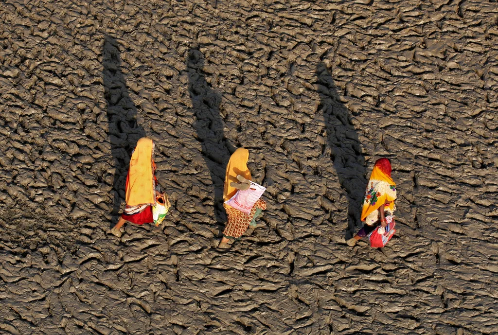 Ženy kráčí po bahnitém břehu Gangy po posvátné koupeli ve městě Iláhábád v Indii.