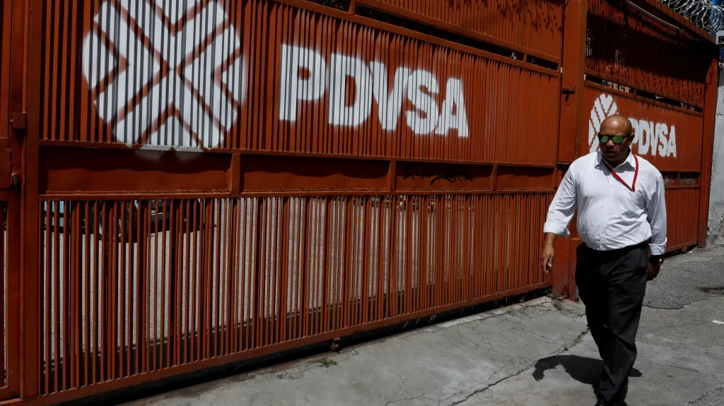 Muž prochází kolem brány s logem venezuelské státní firmy PDVSA