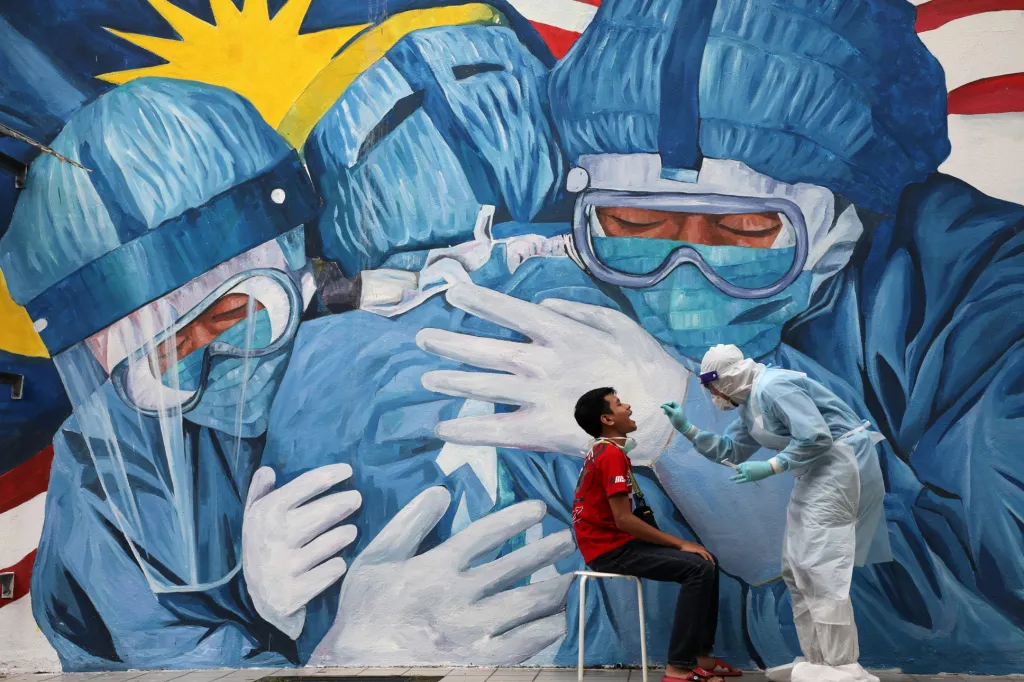 Zdravotník provádí odběr vzorků před obřím graffiti na klinice Ajwa v Shah Alam v Malajsii