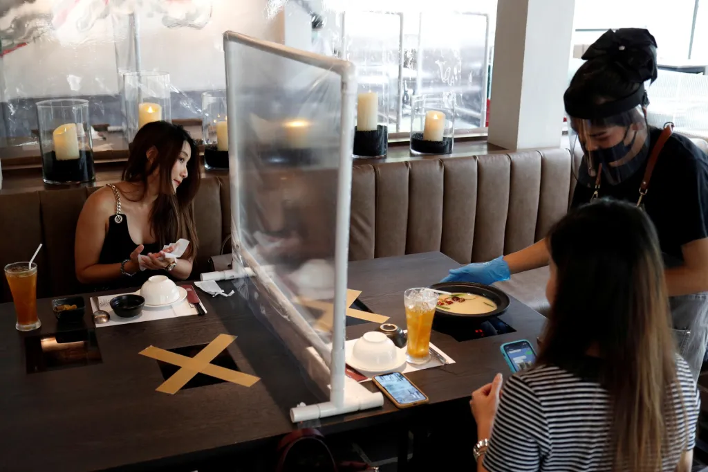 Lidé obědvají v restauraci, která po uvolnění omezení mohla znovu otevřít díky zavedení plastové bariéry