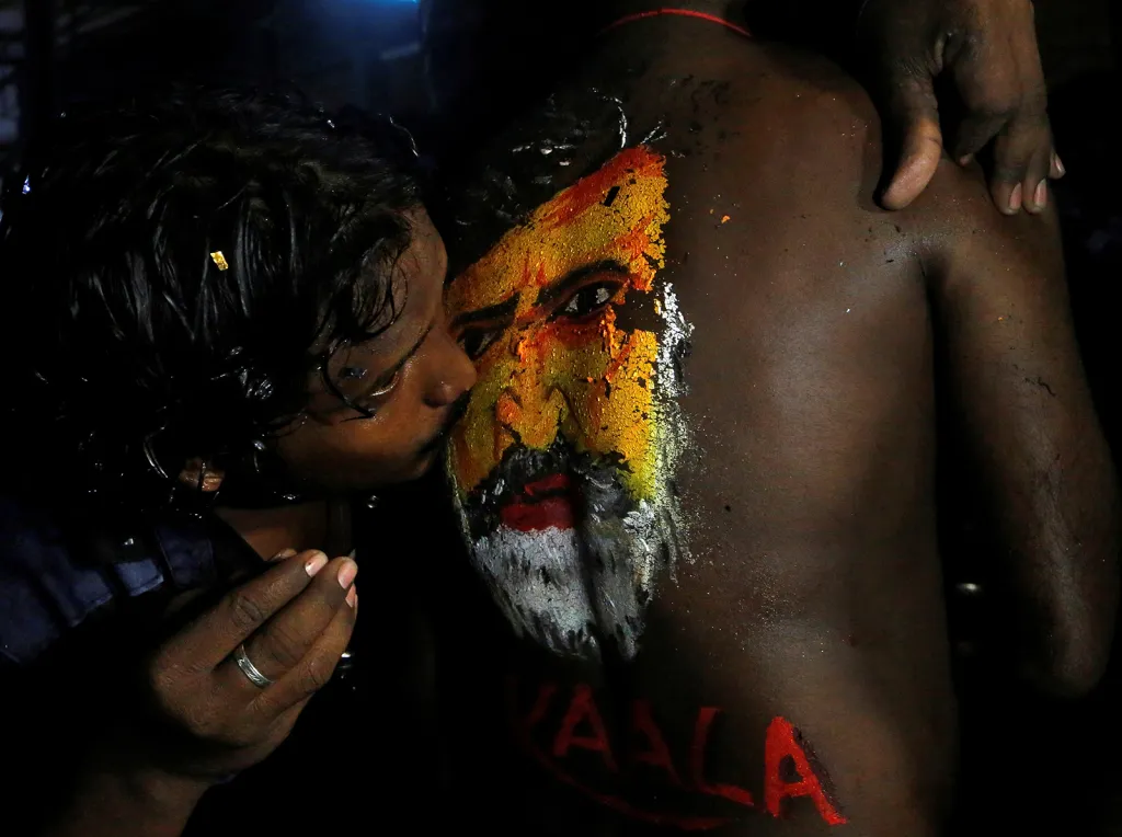 Fanoušek indické filmové hvězdy, herce Rajinikantha, líbá jeho obraz namalovaný na zádech jiného fanouška během oslav při uvedení jeho nového filmu Kaala v indické Bombaji.