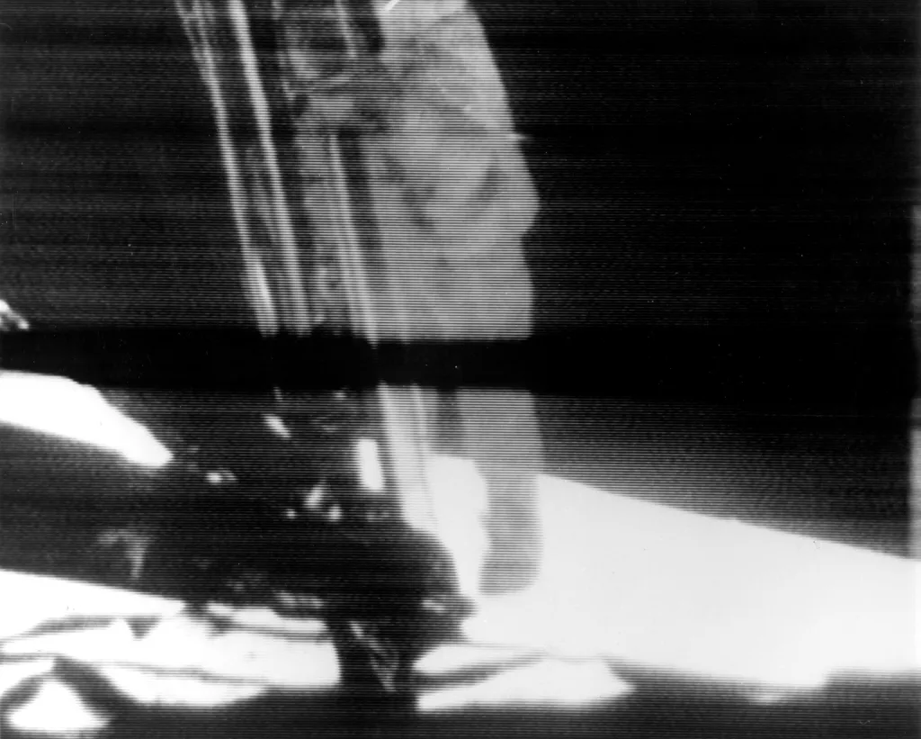 20. července 1969 byl do světa přenášen televizní záznam v momentu, kdy Armstrong sestupuje po žebříku na měsíční povrch. Černý pruh procházející středem fotografie je anomálií v systému televizního přenosu