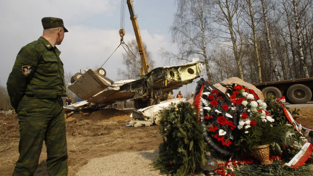 Voják stojí na stráži, zatímco jeřáb zvedá vrak letadla Tupolev Tu-154. Na místě havárie jsou položeny věnce na památku obětí ve Smolensku (14. dubna 2010)