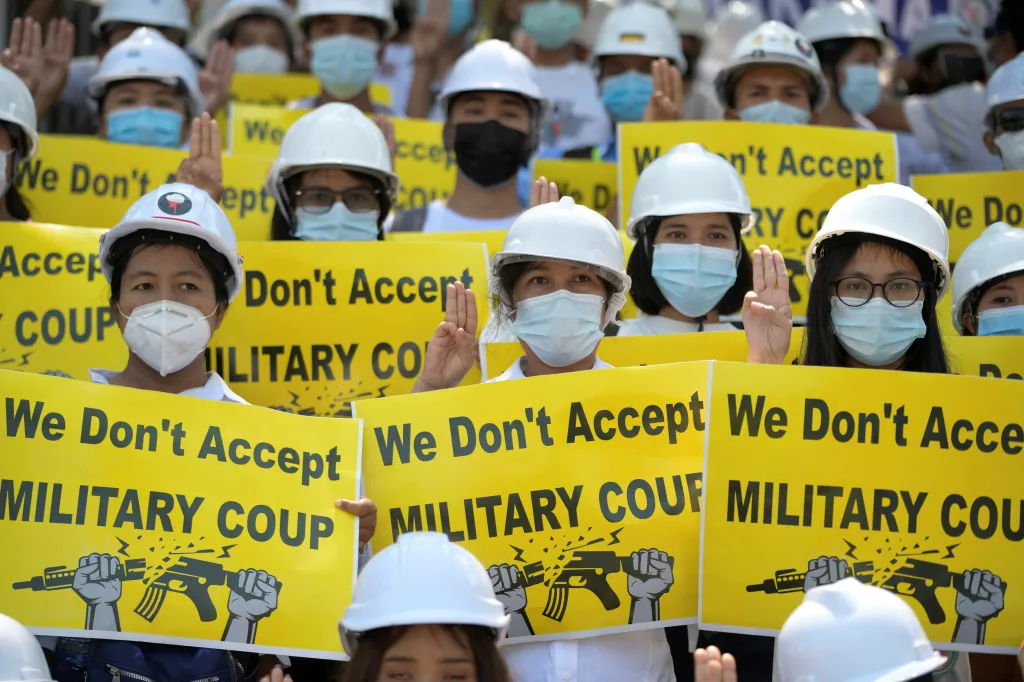 Demonstranti v Rangúnu drží transparenty, na kterých odsuzují řízení země armádou. Pravici mají zdviženou a ukazují tři prsty –⁠ gesto, které je pro region příznačné. Používali jej například protestující v Thajsku. Původně ale pochází z hollywoodského filmu Hunger Games