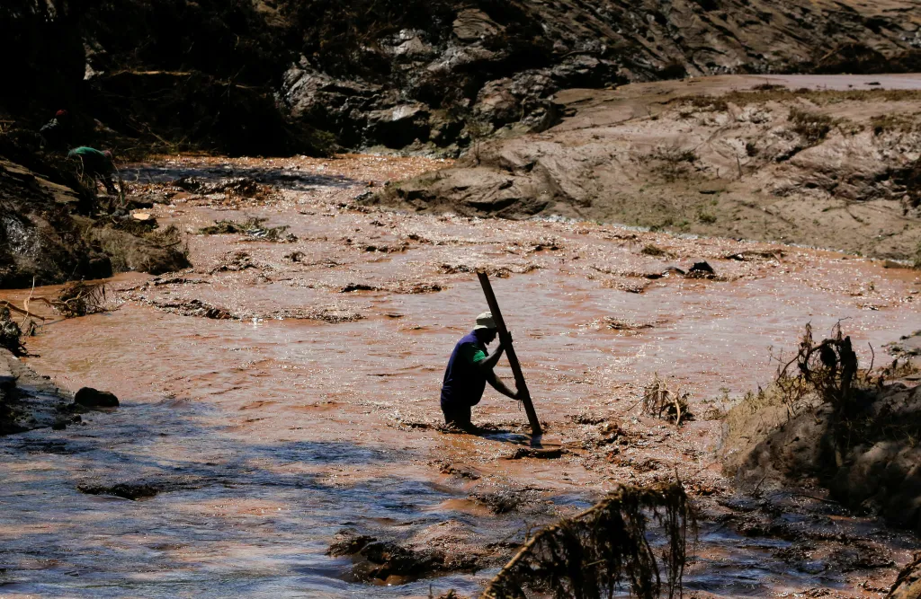 Muž používá hůl k překonání řeky poté, co silné bleskové povodně po prudkých deštích zničily několik domů