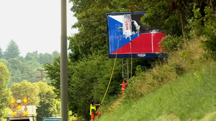 Pracovníci vylepují vlajku na billboard