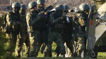 Neoznačení ruští vojáci v úkrytu za obrněným vozidlem ve snaze převzít vojenskou leteckou základnu v krymském městě Belbek nedaleko Sevastopolu 22. března 2014. Velitel základny byl odvezen do Moskvy k rozhovorům poté, co ozbrojené oddíly s automatickými puškami pronikly na její půdu.
