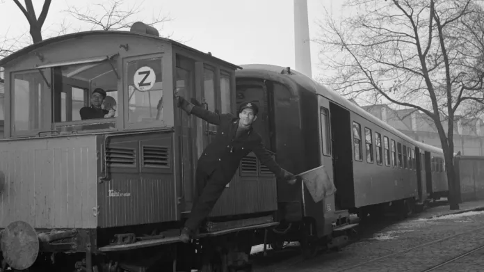 Na snímku z 50. let vyjíždí nově vyrobené vozy z vrat vagonky Tatra Smíchov. Jde o vozy řady Cai, které dnes jezdí na historických vlacích. Za pozornost stojí i akumulátorová lokomotiva v jejich čele